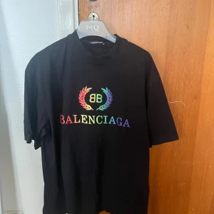 Balenciaga T-shirt - Svart t-shirt från Balenciaga med färgglatt regnbågstryck och logga framtill. Klassisk rund hals och korta ärmar. Skön passform och tillverkad i mjuk bomull. Perfekt statement-plagg för dig som gillar streetstyle och designer. Inget kvitto och därav priset