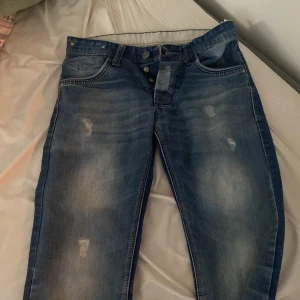 Blå jeans från Armani W33 L34 - Säljer ett par blå jeans från Armani med snyggt slitna detaljer och knäppning med flera knappar. Jeansen har klassisk femficksdesign och en cool tvätt med ljusare partier framtill. Perfekta för dig som gillar en avslappnad och trendig look.