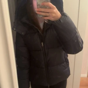 Mörkblå pufferjacka från Nelly XS - Säljer en mörkblå pufferjacka från Nelly i storlek XS. Jackan har huva, dragkedja framtill och två fickor med knappstängning. Perfekt för kalla dagar och har en riktigt snygg, enkel look som passar till det mesta. den är använd en enstaka gång och är i ett superbra skick