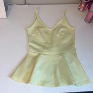 Gult volanglinne - Supersöt ljusgul linne-topp med smala axelband och v-ringning. Toppen har en volang nertill.