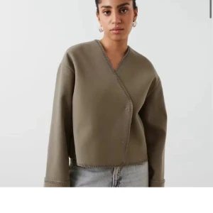 Beige cardigan jacka från Gina tricot - Säljer en beige cardigan jacka med v-ringning och dekorativa sömmar längs kanterna. Koftan har lång ärm och en loose passform, perfekt att slänga på sig över ett linne eller t-shirt. Enkel och stilren design som funkar till det mesta. Har ett litet märke vid armen men syns knappt 