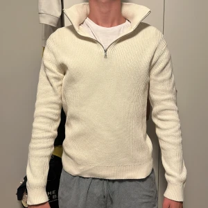 Vit stickad half zip-tröja - Säljer en stilren vit stickad tröja med half zip och hög krage. Tröjan har lång ärm och är ribbstickad vid muddar och nederkant. Perfekt för lager-på-lager och passar till både jeans och mjukisbyxor.