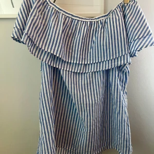 Blåvit offshoulder topp Gina Tricot - Söt randig topp från Gina Tricot med offshoulder och volang upptill. Perfekt för sommardagar, i luftig bomull och med avslappnad passform. Köptes på plick men sedan aldrig använd!