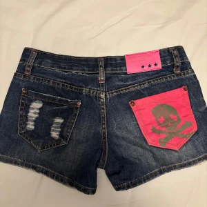 Lowwaist jeansshorts - Mörkblå jeansshorts med slitna detaljer. Ficka med as snyggt rosa tryck. Aldrig använd. Passar Xs/ mindre S. Pris går att diskuteras