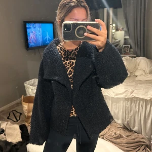 Svart teddyjacka med oversized passform - Mysig svart teddyjacka med bred krage och oversized passform. Jackan har en fluffig struktur och långa ärmar, perfekt för att hålla värmen. Enkel och stilren design som funkar till många outfits.