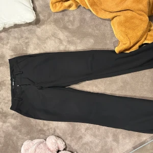 Svarta kostymbyxor från BikBok - Säljer ett par svarta kostymbyxor från BikBok i storlek 34. Byxorna har raka ben, hällor för bälte och klassisk dragkedja framtill. Perfekta för en clean och stilren look. Materialet känns mjukt och följsamt.