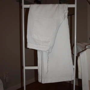 Vita linnebyxor med snörning - Snygga vita linnebyxor med breda raka ben och dragsko i midjan. Byxorna har stora fickor både fram och bak, vilket ger en chill och avslappnad vibe. Perfekta för varma dagar när du vill ha något luftigt och bekvämt.