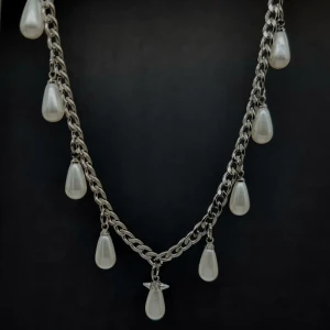 Silverhalsband med droppformade pärlor - Stilrent halsband i silverfärgad metall med kedja och hängande droppformade vita pärlor. Kedjan har ett klassiskt länkmönster och pärlorna ger en elegant och trendig vibe. Perfekt för dig som gillar att sticka ut med detaljer.