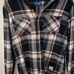 Rutig skjorta från Jack & Jones - Snygg rutig skjorta från Jack & Jones i svart, vit och röd. Skjortan har klassisk krage, knäppning framtill och två bröstfickor. Perfekt för dig som gillar en avslappnad men stilren look.