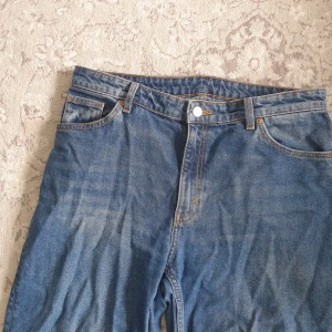 Blå raka jeans - Säljer ett par klassiska blå jeans med rak passform och rå, fransig kant nertill. Jeansen har fem fickor, orange sömmar och är tillverkade i 100% bomull. Perfekta för dig som gillar en avslappnad och tidlös look. Storlek W32