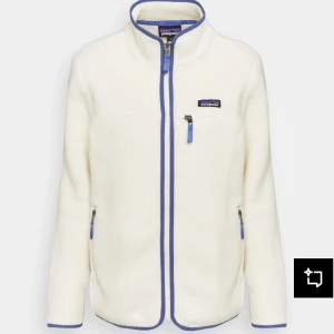 Vit fleecejacka från Patagonia - Mysig vit fleecejacka från Patagonia med blå detaljer och dragkedjor. Jackan har hög krage, bröstficka med dragkedja och två vanliga fickor. Perfekt för kyliga dagar och enkel att styla till det mesta. Nypris 1650kr💕