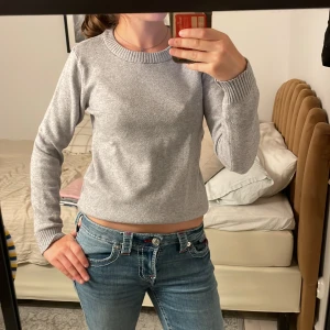 Ljusgrå stickad tröja med rund hals - Enkel och stilren ljusgrå stickad tröja med rund halsringning och ribbade muddar vid ärmslut och nederkant. Perfekt för lager-på-lager och passar till jeans eller kjol. Långärmad och mjuk, passar dig som gillar en clean look.