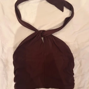 Brun halterneck topp från MNG - Supersnygg brun halterneck topp från MNG med knyt runt nacken och smockad rygg för extra komfort. Toppen är croppad och har en stilren, enkel design som passar perfekt till jeans eller kjol. Mjuk och lätt i materialet, perfekt för varma dagar.