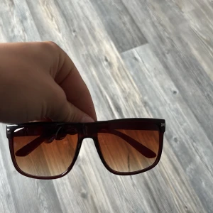 Liknar raybans - Snygga solglasögon i brun transparent plast med fyrkantig form och tonade glas. Perfekta för att ge en cool touch till din stil. Passar dig som gillar klassiska men trendiga accessoarer.
