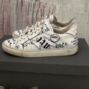 Zadig & Voltaire skor - Unika vita sneakers från Zadig & Voltaire med svart graffiti- och textprint över hela skon. Skorna är väll använda, men fungerar fortfarande till användning! Har även köpt till nya skosnören som inte är använda, som då medföljer! Skorna är i storlek 36. Hör av dig vid frågor. Pris kan diskuteras vid snabb affär!
