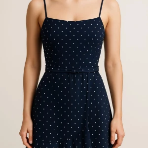 Mörkblå prickig klänning med smala axelband - Säljer en mörkblå klänning med vita prickar och smala axelband. Klänningen har ett bälte i midjan och är i en lätt, luftig modell som passar perfekt till varma dagar. Prickigt mönster ger en söt och tidlös look.