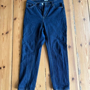 Mörkblå högmidjade jeans - Säljer ett par mörkblå jeans med klassisk femficksdesign och raka ben. Jeansen har hög midja och tydliga kontrastsömmar. Storlek 46.