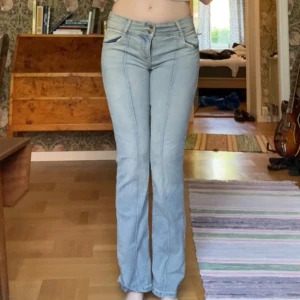 Ljusblå bootcut jeans från Bershka - Säljer ett par ljusblå bootcut jeans från Bershka med dubbla knappar och klassiska fickor både fram och bak. Jeansen har låg midja och är tillverkade i denim med snygga sömdetaljer. Perfekta för dig som gillar en retro vibe. Har använt Max 2 gånger, tvättade en gång. Lite för små för mig.