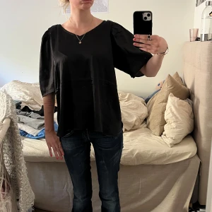 Svart blus från Isolde - Säljer en svart blus från Isolde med v-ringning och korta, lätt puffade ärmar. Blusen har en lös passform och är tillverkad i ett glansigt, mjukt material som ger en elegant känsla. Perfekt att styla med jeans eller kjol. Den är i stl L men ni kan ju se på bilden hur den sit tre r på mig som är XS/S. Säljer då jag aldrig andvänt den.