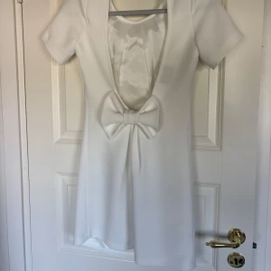 Student klänning öppen rygg - Säljer en elegant vit kortklänning från Ellaluna med djup rygg och stor rosettdetalj baktill. Superfin till studenten, kan mötas upp eftersom de är lite sista minuten! Står heller inte storlek men passar nog s-m 