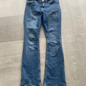 Blå bootcut jeans - Säljer ett par klassiska blå bootcut jeans med normal passform. Jeansen har fem fickor och stängs med dragkedja och knapp. Perfekta till vardags för en avslappnad men ändå trendig look.