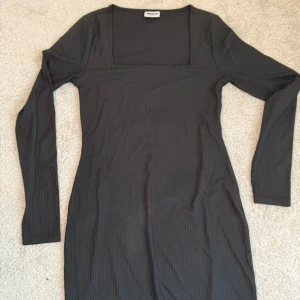 Svart ribbad långärmad klänning från Noisy May - En svart, ribbad klänning från Noisy May med lång ärm och fyrkantig ringning. Klänningen har en tight passform och är perfekt för dig som gillar en enkel men stilren look.