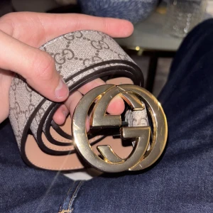 Gucci GG Supreme bälte med guldspänne - Säljer ett Gucci GG Supreme bälte med klassiskt mönster och stort guldigt GG-spänne. Bältet är beige med bruna detaljer och har en exklusiv känsla. Perfekt accessoar för att lyfta din outfit. Bältet är storlek 100 