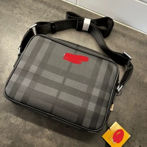 Svart axelväska med rutigt mönster - Snygg svart axelväska med diskret rutigt mönster och justerbar axelrem. Väskan har dragkedja upptill, ett ytterfack med dragkedja och flera innerfack för enkel organisering. Perfekt för att bära det viktigaste i vardagen.