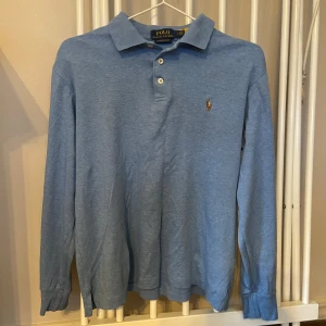 Ljusblå pikétröja från Polo Ralph Lauren - Säljer en ljusblå långärmad pikétröja från Polo Ralph Lauren. Tröjan har klassisk krage, tre knappar och loggan på bröstet. Modellen är custom slim fit och passar S-XS.