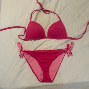 Rosa Calzedonia bikini med knyt - Säljer en snygg rosa bikini från Calzedonia med trekants-bh och knyt i sidorna på underdelen. Bikinin har två olika nyanser av rosa och är perfekt för stranden eller poolen. Materialet är mjukt och stretchigt syntet. Aldrig använd
