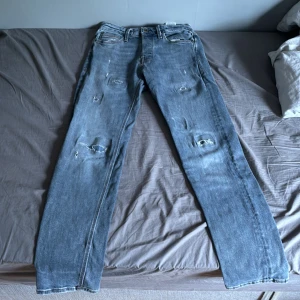 Ljusblå slitna jeans från Jack & Jones - Säljer ett par ljusblå jeans från Jack & Jones med slitna detaljer och raka ben. Klassisk femficksmodell med läderpatch bak i midjan. Perfekta för en avslappnad stil.