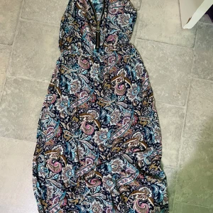 Mönstrad långklänning med dragkedja - Säljer en långklänning med färgstarkt paisleymönster i blått, rosa, brunt och vitt. Klänningen har ärmlös design och en synlig dragkedja framtill. Perfekt för dig som gillar bohemisk stil och vill sticka ut.