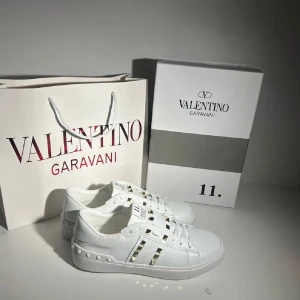 Vita sneakers Valentino Garavani - Snygga vita sneakers från Valentino Garavani med ikoniska nitar längs sidorna och diskreta detaljer. Skorna har rund tå och platt sula, perfekt för en trendig och stilren look.