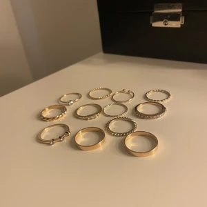 Set med guldiga ringar - Säljer ett set med tolv stilrena guldiga ringar i olika designer. Vissa ringar har små pärldetaljer och andra är släta eller med räfflad kant. Perfekta att mixa och matcha för en trendig look.