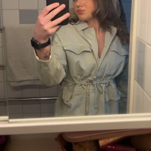 Ljusgrön utilityjacka från ZARA - Säljer en ljusgrön utilityjacka från ZARA med knappar och dragsko i midjan. Jackan har stora fickor framtill och klassisk krage. Perfekt för lager-på-lager och enkel att styla till olika outfits.