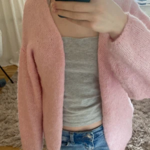 Ljusrosa stickad kofta - Mysig ljusrosa stickad kofta med lång ärm och öppen framtill. Koftan har en avslappnad passform och är perfekt att slänga på sig över en topp. Passar till jeans eller kjol för en chill look.