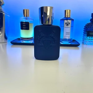 Layton Eau de Parfum från Parfums de Marly - Exklusiv herrparfym i en matt mörkblå flaska med silverfärgat lock. Flaskan har ingraverade hästar och sköld på framsidan. Innehåller 75 ml Eau de Parfum med en elegant och lyxig känsla. Perfekt för dig som gillar unika och sofistikerade dofter. Ca 25% kvar