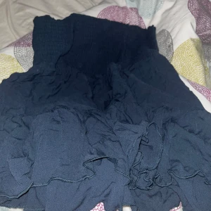 Mörkblå volangkjol - Supersöt mörkblå kjol med volanger och smock i midjan. Kjolen är kort och har en luftig känsla, perfekt för varmare dagar. Enkel att matcha med olika toppar för en trendig look. Helt ny 