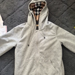 Grå hoodie med rutigt foder - Säljer en grå burberry kofta, helt ny, passar M/L, 1399kr