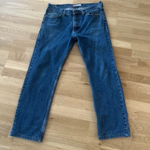 Levi's 501 blå jeans - Klassiska blå Levi's 501 jeans med raka ben och femficksmodell. Byxorna har normal passform och är tillverkade i slitstarkt denimtyg. Perfekta för dig som gillar tidlös stil och vill ha ett par jeans som funkar till det mesta.