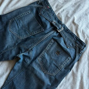 Mörkblå jeansbyxor från Diesel - Säljer ett par aödrig använda mörkblå jeansbyxor från Diesel med klassisk femficksdesign och snygga detaljer som dragkedja på myntfickan.  Jeansen har raka ben och subtila slitningar för en cool  look. Perfekta till vardags för en avslappnad stil. Midja: 44cm Längd:106cm Benslut:24cm