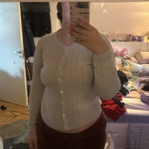 Vit kabelstickad kofta från XOXO friends - Säljer en vit kabelstickad kofta från XOXO friends. Koftan har rund halsringning, långa ärmar och knäppning framtill med vita knappar. Perfekt för lager-på-lager och enkel att matcha med olika outfits.