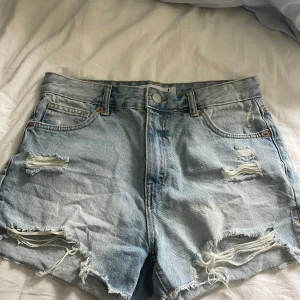 Ljusblå jeansshorts från FB Sister - Säljer ett par ljusblå jeansshorts från FB Sister i storlek L. Shortsen har slitna detaljer, fransiga benslut och klassisk femficksdesign. De har normal passform och stängs med dragkedja och knapp. Perfekta för sommaren! Sitter mer som M!