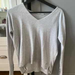 Ljusgrå v-ringad tröja  - Säljer en ljusgrå v-ringad tröja. Tröjan har lång ärm och ribbade muddar vid ärmslut och nederkant. Perfekt för lager-på-lager och enkel att matcha med olika outfits.