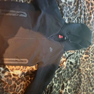 Svart hoodiejacka från Nike - Säljer en svart hoodiejacka från Nike med dragkedja och två fickor framtill. Jackan har en sportig look med diskret Nike-logga på bröstet och huva. Perfekt för dig som gillar enkel och stilren design.