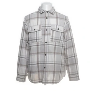 Beige och vit rutig skjorta med fickor - Säljer en stilren rutig skjorta i beige och vitt med två bröstfickor och knäppning framtill. Skjortan har klassisk krage och långa ärmar, perfekt för en avslappnad men snygg look. Från hm