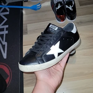 Golden Goose - Svarta sneakers från Golden Goose med vit stjärndetalj på sidan och vit häl. Skorna har svarta skosnören, svart ovandel och vit sula. Märket syns tydligt på plösen och innersulan. Klassisk och stilren modell. Riktigt schyssta skor till sommarn om du skulle fråga mig. Säljer för jag letar nytt, använda ksk 10-15 gånger max helt nya typ. Öppen mot byten hör av er 😜✌️💫 köpte för 2200 av en annan snubbe men lite lägre pris då dom är använda det följer även med en dustbag också 