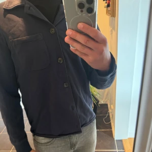 Mörkblå overshirt från Riley - Säljer en stilren mörkblå overshirt från Riley i storlek M passar även S. Overshirten har klassisk krage, bröstficka och knäppning framtill med stora knappar. Hör av er för eventulla frågor!!
