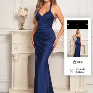 Marinblå långklänning med slits - Säljer en elegant marinblå långklänning med halterneck och djup v-ringning. Klänningen har en smickrande drapering över magen och en hög slits framtill. Perfekt för bal eller fest. Materialet har en lätt glansig finish. Nypris,500