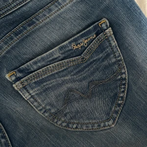 Blå Pepe Jeans bootcut jeans - Säljer ett par klassiska blå jeans från Pepe Jeans med bootcut passform. Jeansen har snygga detaljer på fickorna och en normal midja. Perfekta till en avslappnad stil och passar till det mesta.